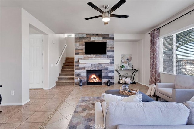 tiled living room with stairway, ceiling fan, baseboards, and a stone fireplace