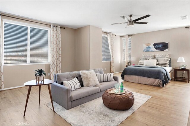 bedroom with a ceiling fan, visible vents, baseboards, and wood finished floors