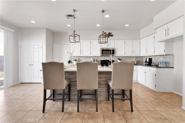 kitchen featuring stainless steel microwave, stove, visible vents, and white cabinetry