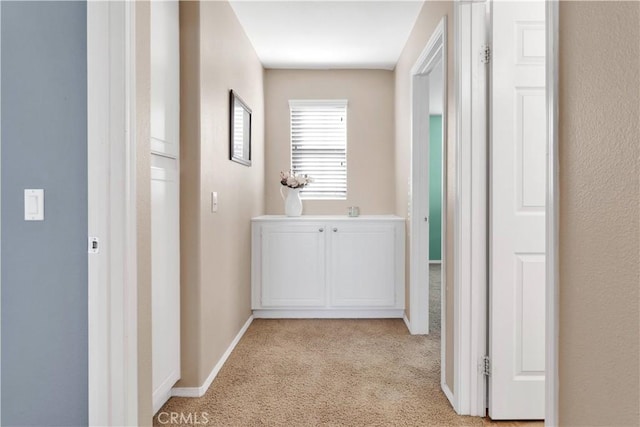 corridor featuring light colored carpet and baseboards