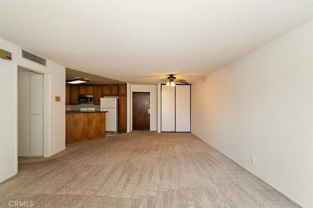 unfurnished living room with ceiling fan, visible vents, a textured ceiling, and light colored carpet