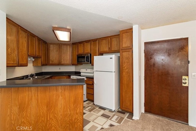 kitchen featuring dark countertops, white appliances, a peninsula, and brown cabinets