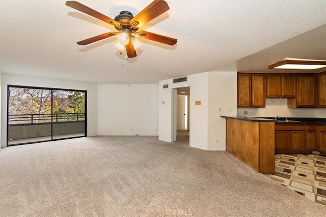 kitchen featuring light carpet, brown cabinetry, dark countertops, ceiling fan, and open floor plan