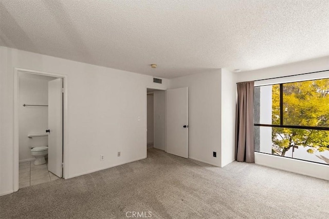 unfurnished bedroom with light colored carpet, connected bathroom, visible vents, and a textured ceiling