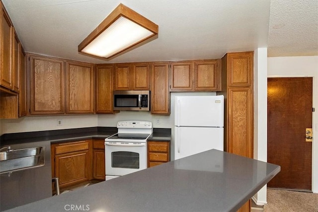 kitchen with brown cabinets, dark countertops, a sink, a textured ceiling, and white appliances