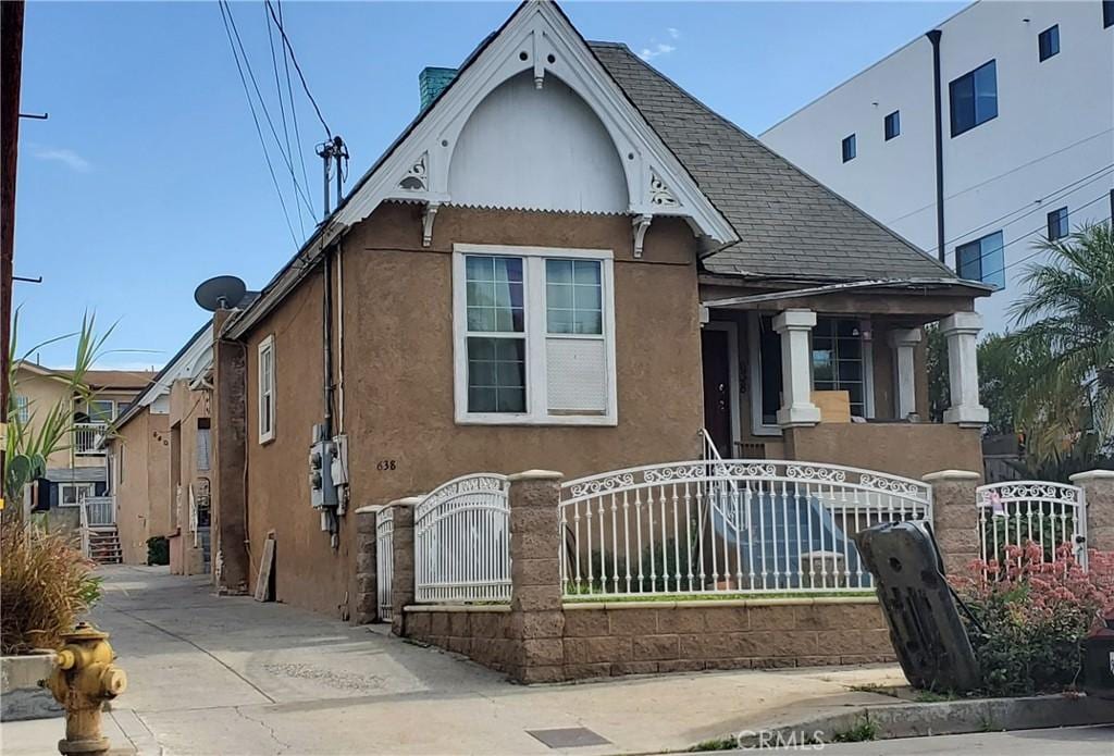 view of front of property with a fenced front yard, a gate, roof with shingles, and stucco siding