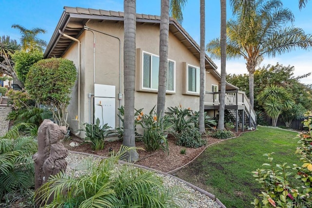 view of side of home featuring stairs, a yard, a wooden deck, and stucco siding