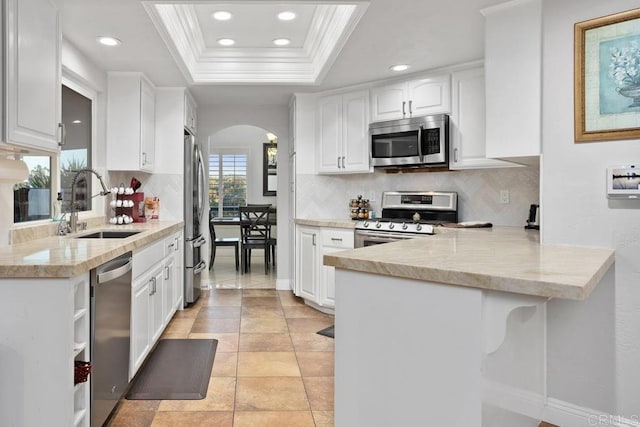 kitchen featuring a tray ceiling, arched walkways, appliances with stainless steel finishes, white cabinets, and a peninsula