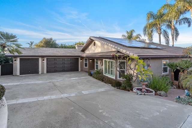 view of front of home with a garage, driveway, a tile roof, roof mounted solar panels, and stucco siding