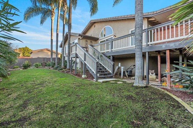 back of house with a lawn, stairs, fence, a wooden deck, and stucco siding