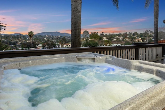 pool at dusk featuring a hot tub and a mountain view