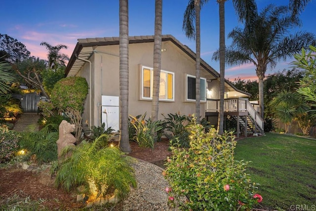 property exterior at dusk featuring stairs, a yard, a wooden deck, and stucco siding