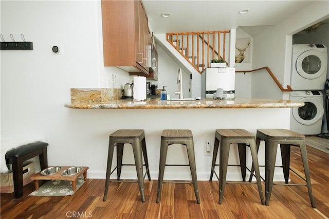 kitchen featuring a peninsula, wood finished floors, a kitchen bar, and stacked washer and clothes dryer