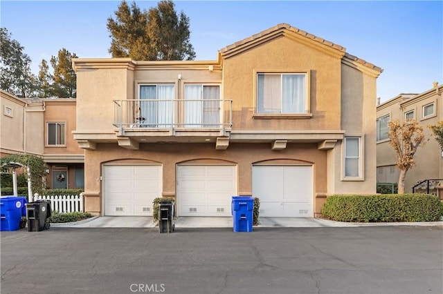 townhome / multi-family property featuring a garage, aphalt driveway, a balcony, and stucco siding