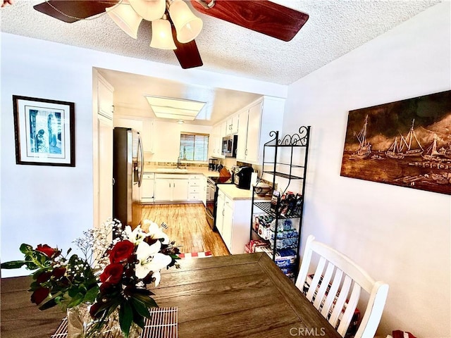 dining space with light wood-style floors, a ceiling fan, and a textured ceiling