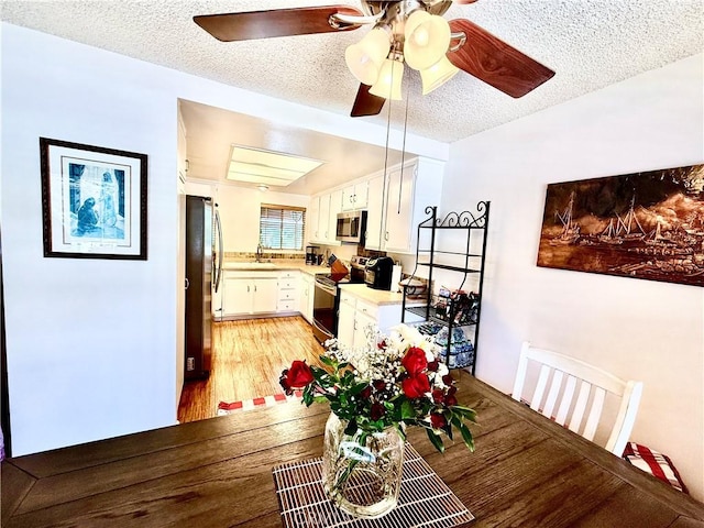 dining area featuring a ceiling fan, light wood-type flooring, and a textured ceiling