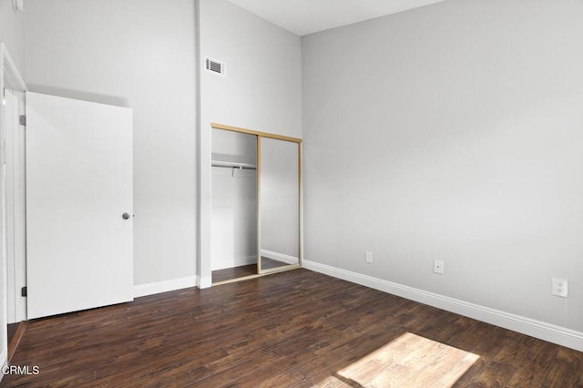 unfurnished bedroom with dark wood-style flooring, a closet, visible vents, and baseboards