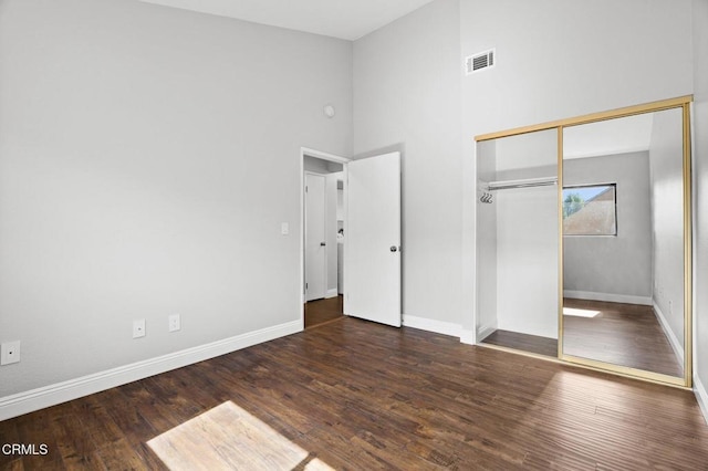 unfurnished bedroom with dark wood-type flooring, a towering ceiling, visible vents, baseboards, and a closet