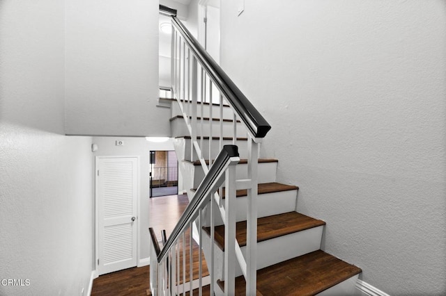 stairway featuring a textured wall, a towering ceiling, baseboards, and wood finished floors