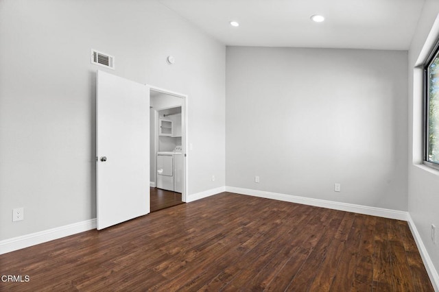 unfurnished room with dark wood-style floors, washing machine and dryer, visible vents, and baseboards