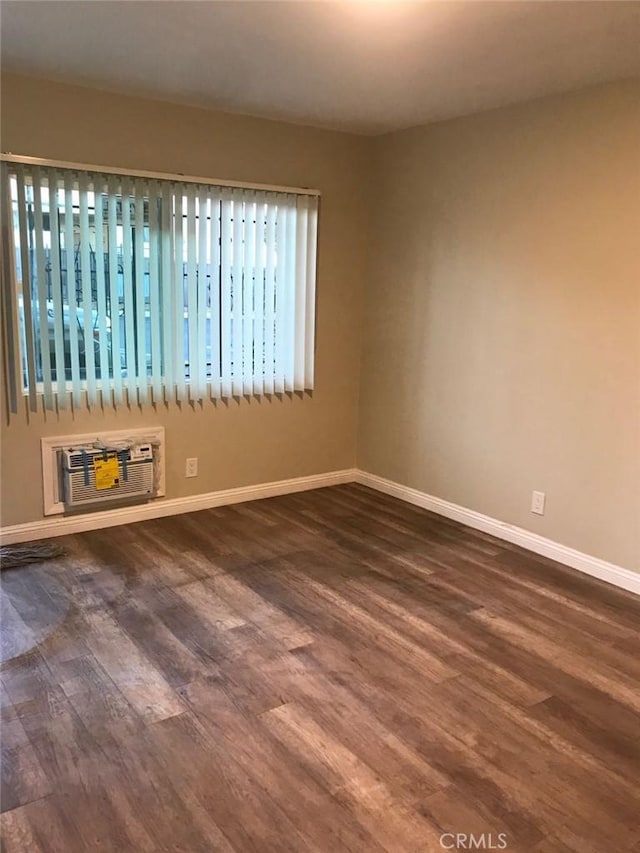 unfurnished room with dark wood-style floors, a wall unit AC, and baseboards