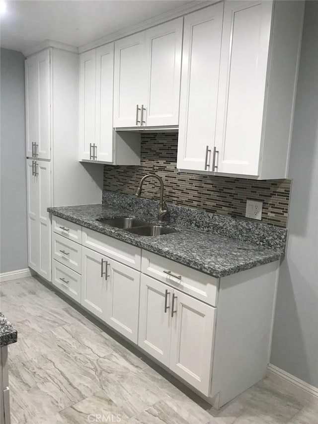 kitchen with dark stone counters, white cabinetry, and a sink