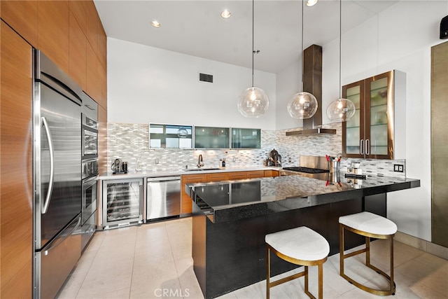 kitchen featuring glass insert cabinets, a peninsula, a kitchen bar, and wall chimney range hood