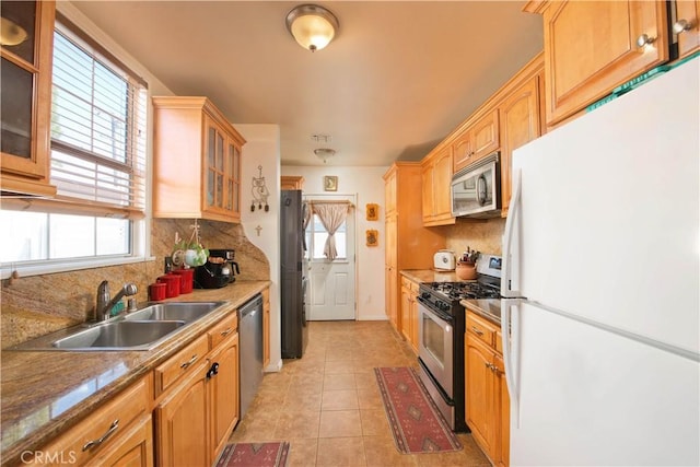 kitchen with light tile patterned floors, glass insert cabinets, a sink, stainless steel appliances, and backsplash