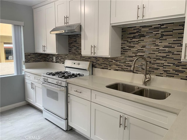 kitchen featuring white gas range, light countertops, under cabinet range hood, white cabinetry, and a sink