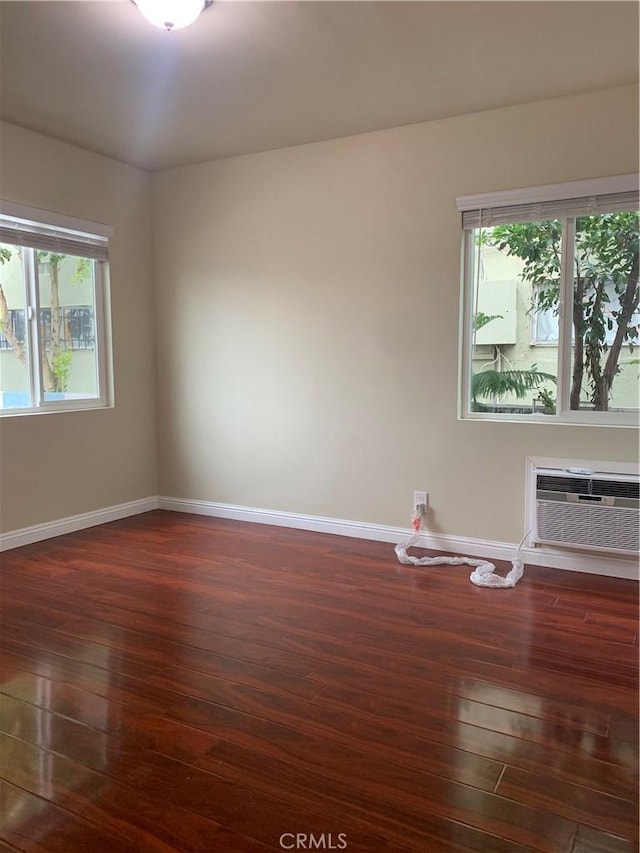 unfurnished room featuring baseboards, dark wood finished floors, and a wall mounted air conditioner