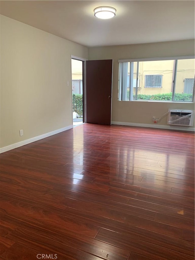 unfurnished room with dark wood-style flooring, a wall mounted AC, and baseboards