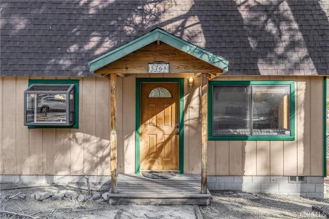 view of exterior entry with roof with shingles and mansard roof