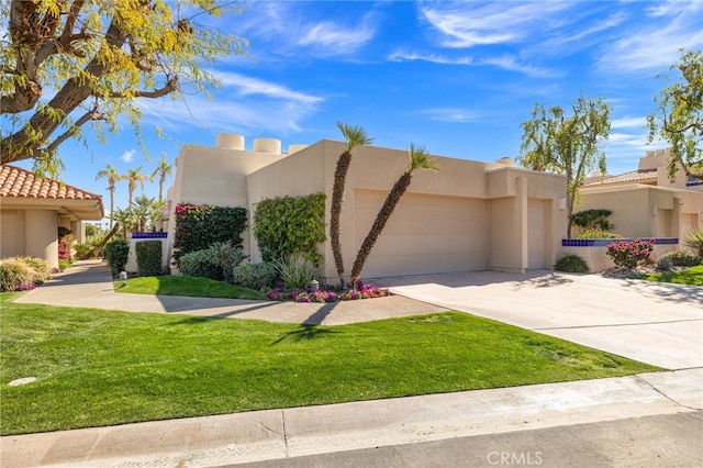 pueblo-style house featuring a garage, a front yard, concrete driveway, and stucco siding