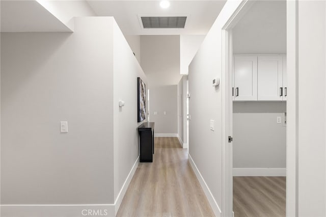 hall with light wood-style flooring, visible vents, and baseboards