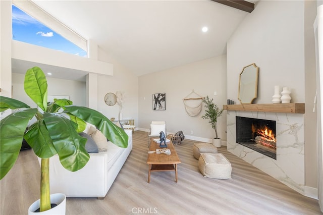 living area featuring baseboards, high vaulted ceiling, a high end fireplace, and light wood-style floors