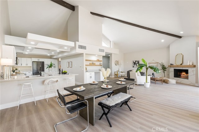 dining room featuring a lit fireplace, visible vents, light wood-style flooring, and beamed ceiling