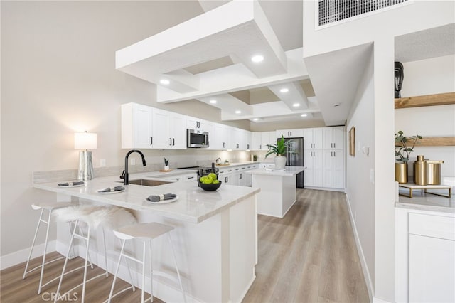 kitchen featuring a breakfast bar, appliances with stainless steel finishes, white cabinetry, a sink, and a peninsula