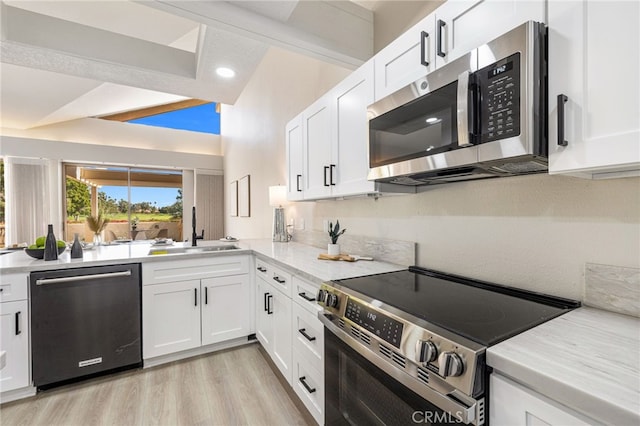 kitchen featuring stainless steel appliances, a sink, light wood-style floors, white cabinets, and decorative backsplash