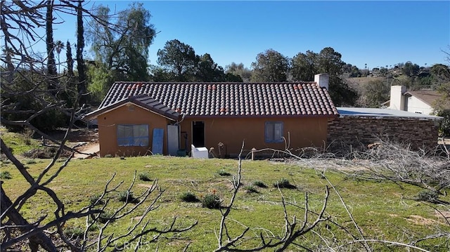 rear view of house featuring a yard, a chimney, a tile roof, and stucco siding