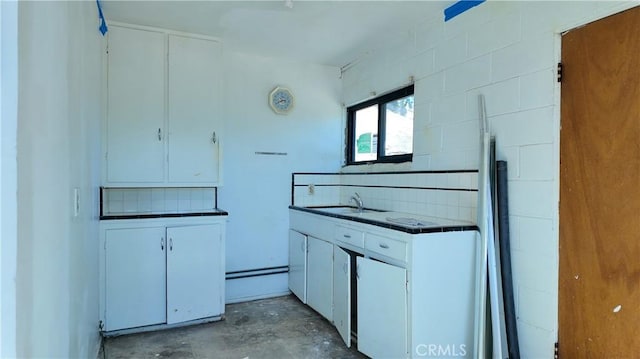 kitchen with concrete flooring, white cabinetry, a sink, and backsplash