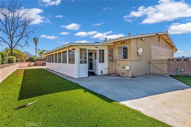 rear view of property with stucco siding, a lawn, a sunroom, a patio area, and fence