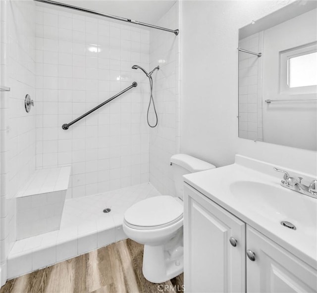 bathroom with toilet, a tile shower, wood finished floors, and vanity