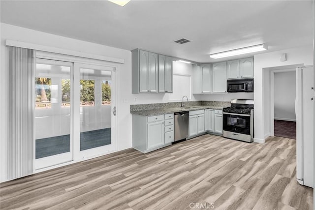 kitchen with white cabinets, light wood finished floors, stainless steel appliances, and a sink