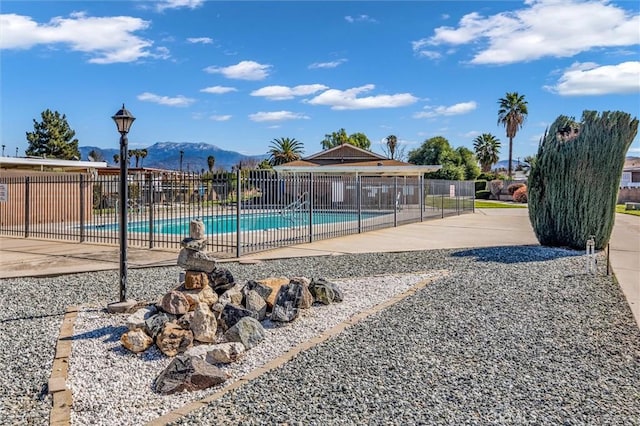 community pool with a patio area, fence, and a mountain view