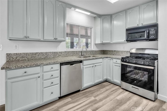 kitchen with light stone counters, stainless steel appliances, a sink, white cabinetry, and light wood-type flooring