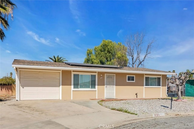 ranch-style home featuring a garage, driveway, roof mounted solar panels, and stucco siding