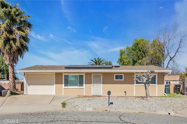 ranch-style home with an attached garage, driveway, solar panels, and stucco siding