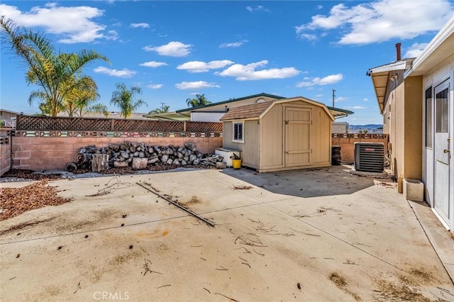 view of patio / terrace featuring an outbuilding, central AC, a fenced backyard, and a storage unit