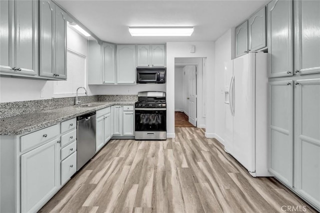 kitchen with baseboards, appliances with stainless steel finishes, light stone counters, light wood-type flooring, and a sink