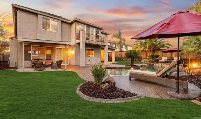 back of property at dusk with a fenced backyard, a balcony, outdoor lounge area, stucco siding, and a patio area